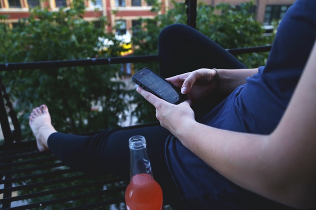 Žena relaxuje na balkóne a hrá sa s mobilom